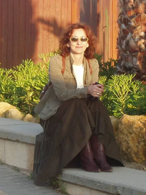 Femme assise sur un muret en extérieur, lunettes de soleil et veste kaki